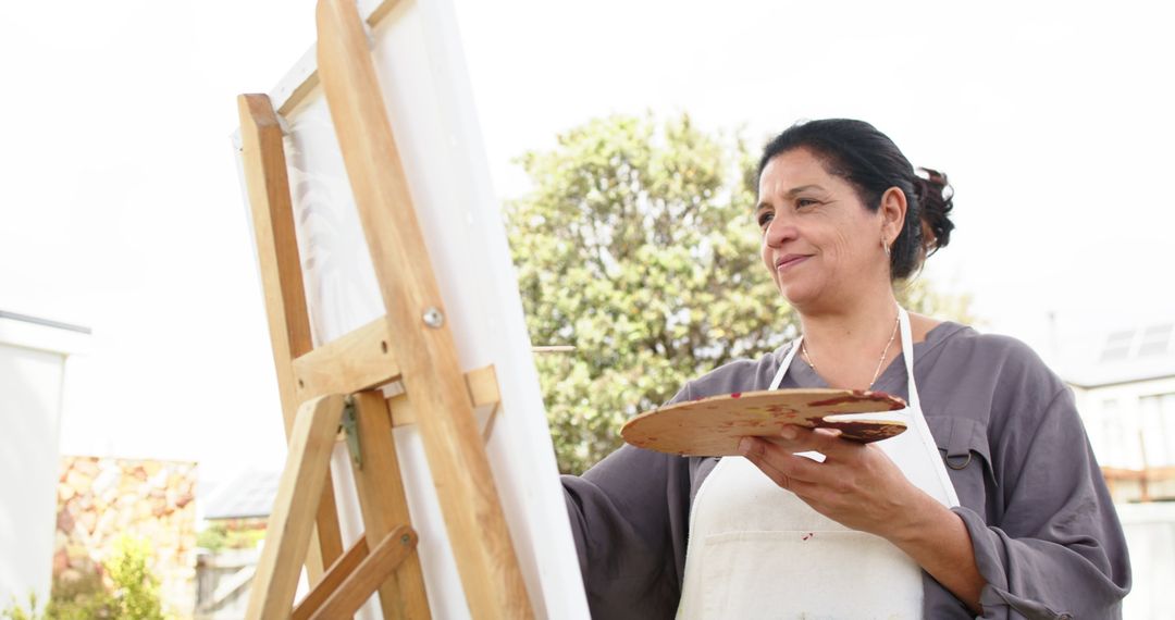 Middle-aged female artist painting outdoors on sunny day - Free Images, Stock Photos and Pictures on Pikwizard.com