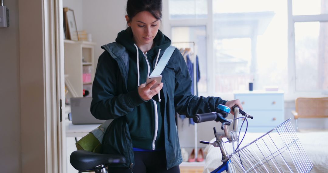 Young Woman Checking Smartphone While Holding Bicycle Indoors - Free Images, Stock Photos and Pictures on Pikwizard.com