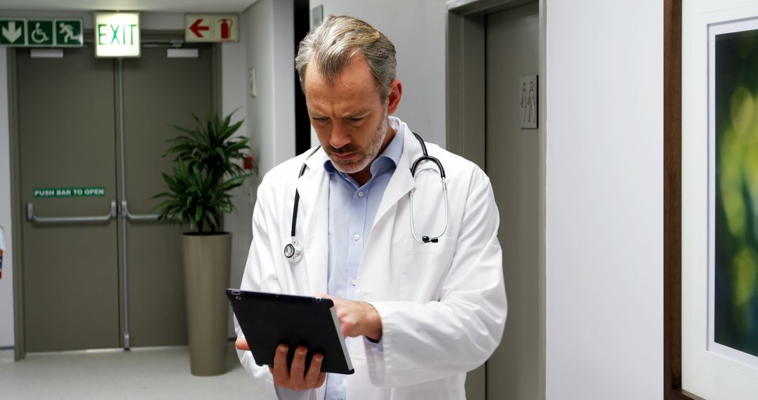 Doctor Reviewing Patient File on Tablet in Hospital Corridor - Free Images, Stock Photos and Pictures on Pikwizard.com