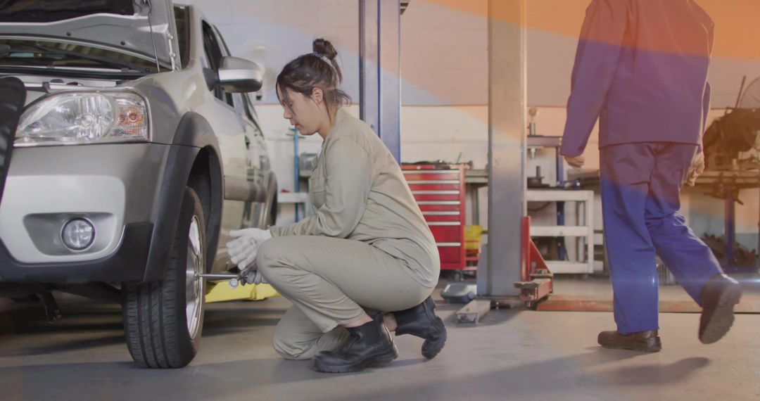 Female mechanic tightening lug nuts on silver SUV wheel in busy automotive workshop