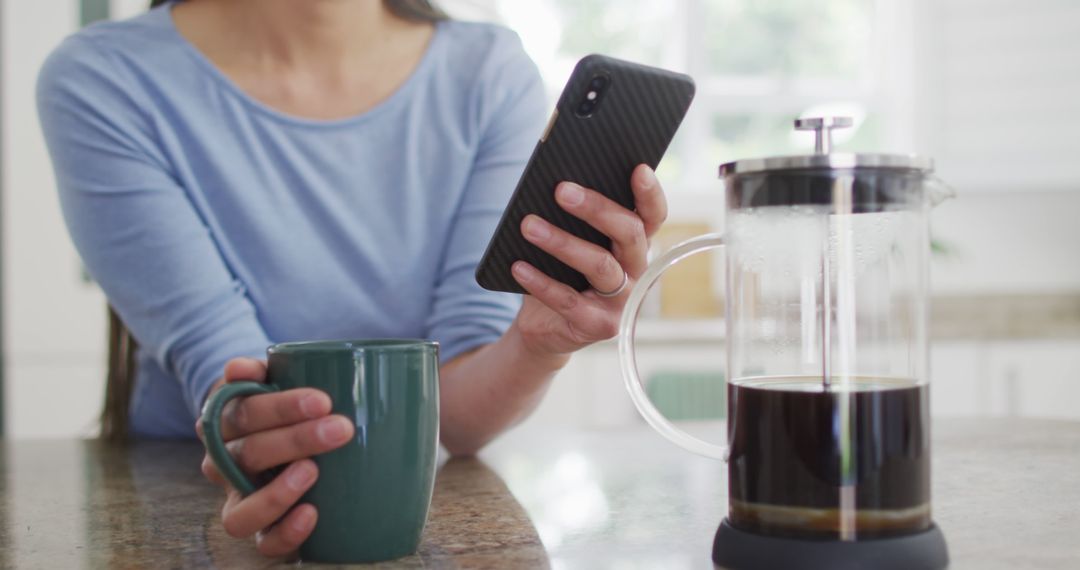 Woman sipping coffee while browsing smartphone in modern kitchen - Free Images, Stock Photos and Pictures on Pikwizard.com