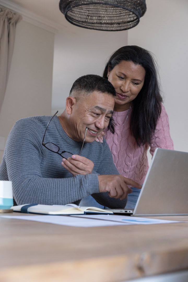 Diverse Senior Couple Smiling and Discussing While Using Laptop