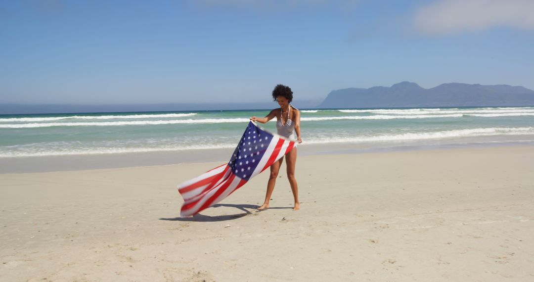 A joyful African American woman celebrates patriotism on a beach with the American flag. - Free Images, Stock Photos and Pictures on Pikwizard.com