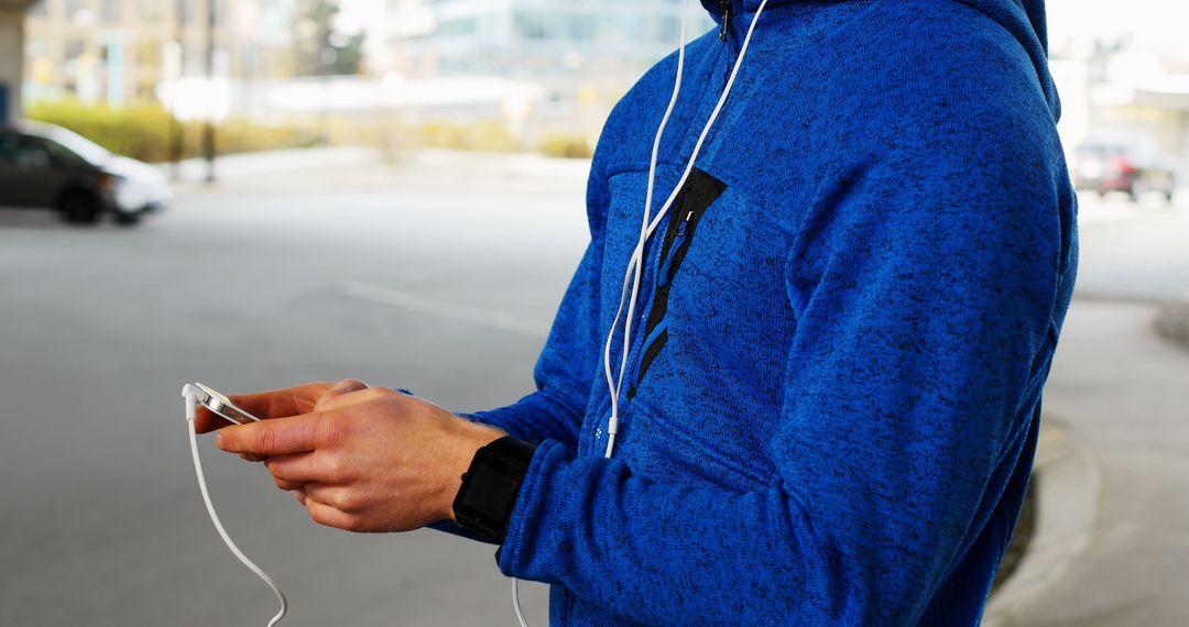 Person in blue hoodie using smartphone with earphones outdoors - Free Images, Stock Photos and Pictures on Pikwizard.com