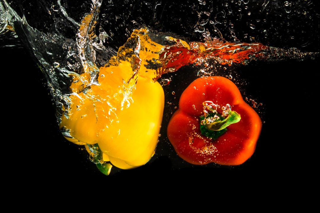 Yellow and Red Bell Peppers Splashing in Water on Black Background