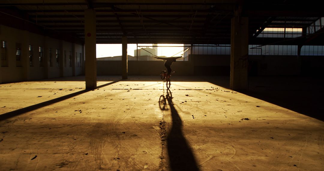 Silhouette of Person Riding Bicycle in Empty Warehouse at Sunset - Free Images, Stock Photos and Pictures on Pikwizard.com