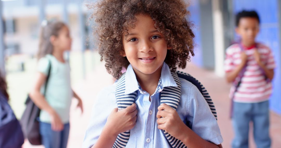 Happy Schoolboy Holding Backpack in Hallway with Classmates