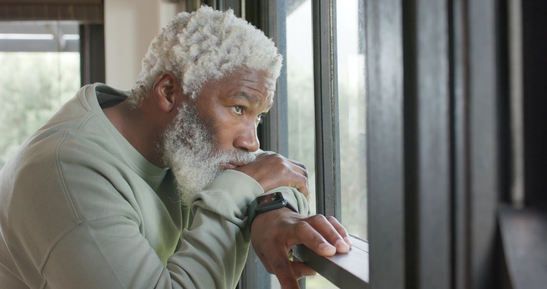 Thoughtful Senior Man Looking Out Window Wearing Smartwatch