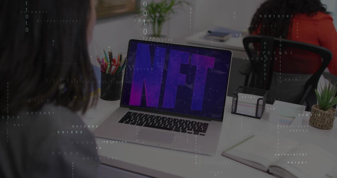 Two women working at modern coworking desk displaying NFT on laptop, digital collaboration