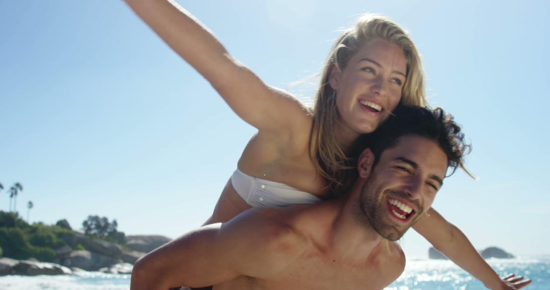 Happy couple enjoying beach piggyback ride under sunny skies - Free Images, Stock Photos and Pictures on Pikwizard.com