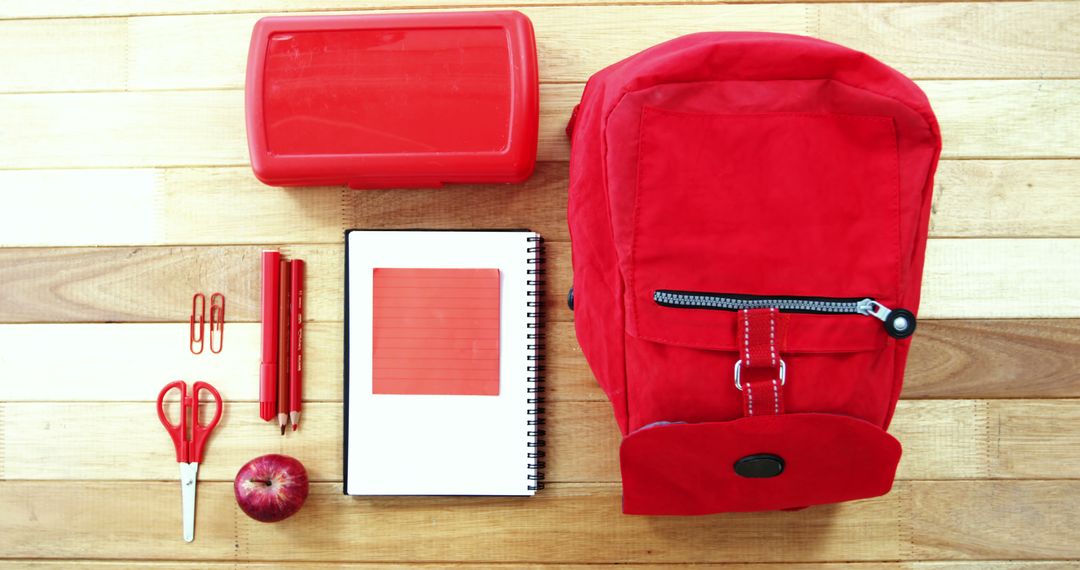Red Backpack and School Supplies Organized on Wooden Floor
