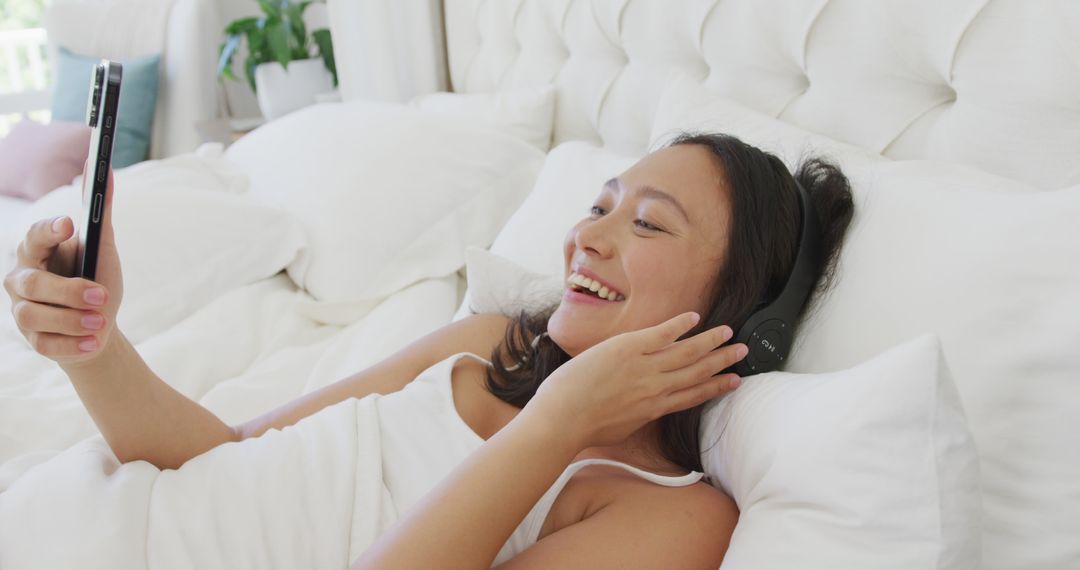 Woman Relaxing in Bed with Smartphone and Headphones, Smiling - Free Images, Stock Photos and Pictures on Pikwizard.com