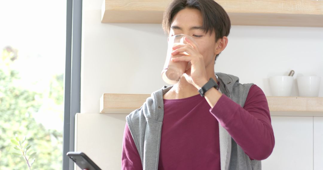 Young Man Enjoys Morning Drink While Using Smartphone at Home
