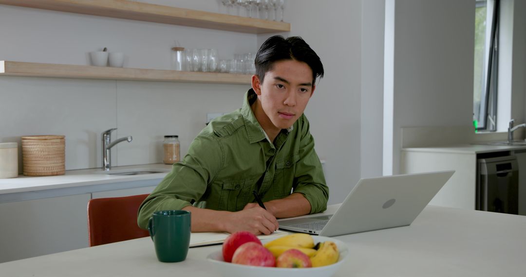 Focused Young Man Working from Home with Laptop and Notepad