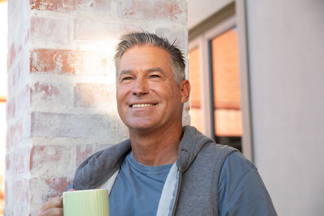 Middle-aged Man Relaxing on Porch Holding Mug by Brick Pillar