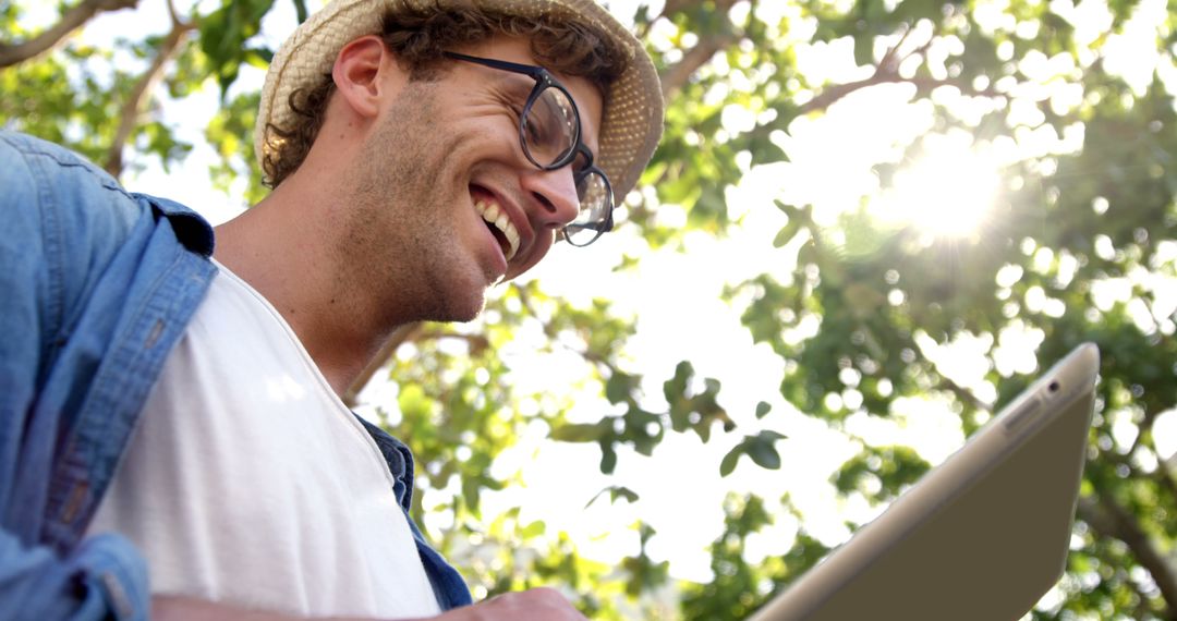 A young Caucasian man smiles as he uses a tablet outdoors, with copy space - Free Images, Stock Photos and Pictures on Pikwizard.com
