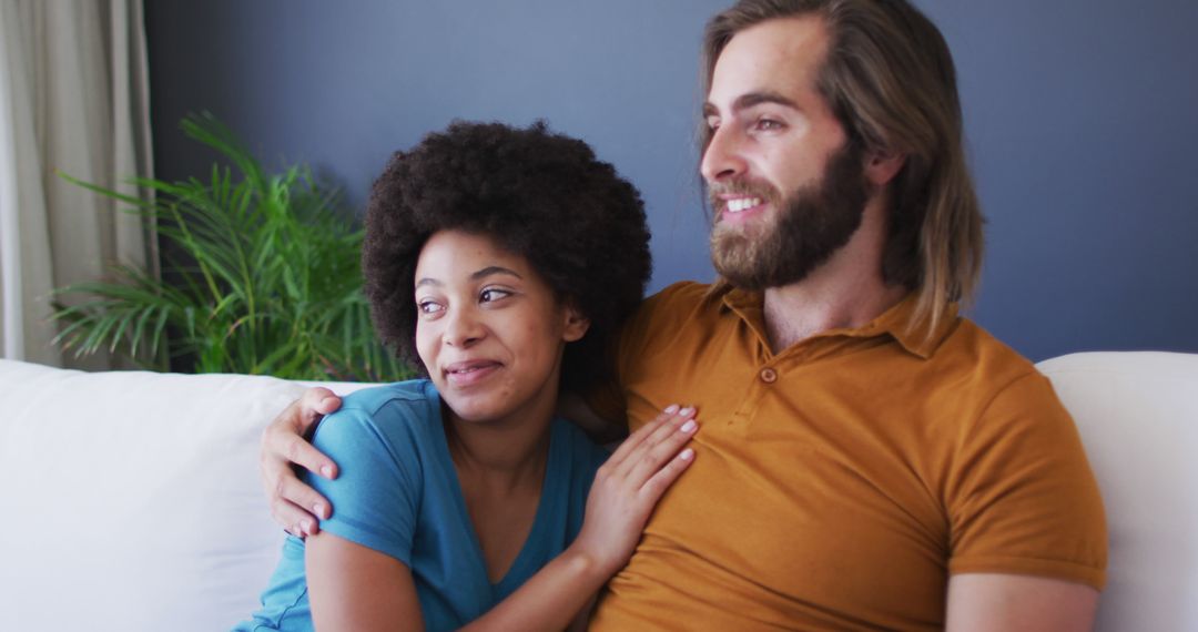 Biracial couple embracing each other while sitting on the couch at home - Free Images, Stock Photos and Pictures on Pikwizard.com