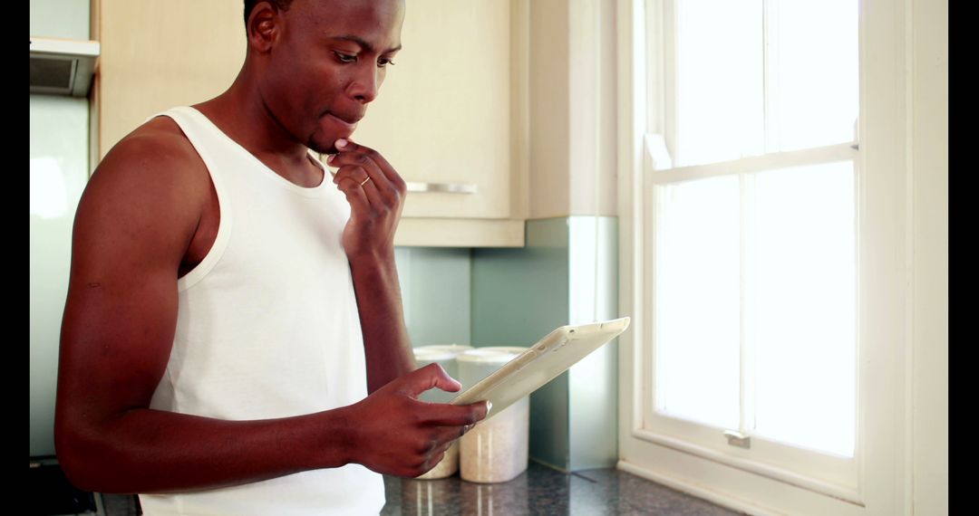 African American Man Using Digital Tablet and Eating in Kitchen - Free Images, Stock Photos and Pictures on Pikwizard.com