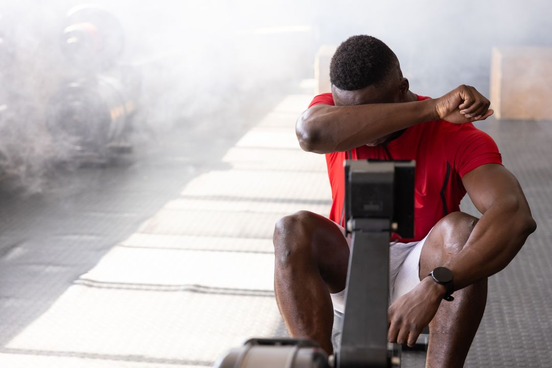 Athlete Resting on Rowing Machine in Smoky Gym Environment