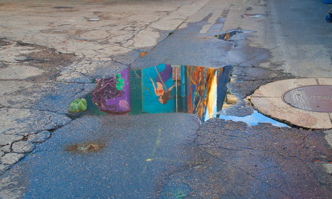 Puddle Reflection of Street Art on Cracked Urban Alleyway - Free Images, Stock Photos and Pictures on Pikwizard.com