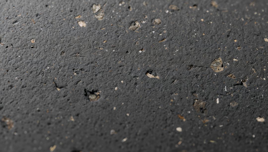 Close-up asphalt surface revealing embedded aggregate and mica flecks, gritty macro texture