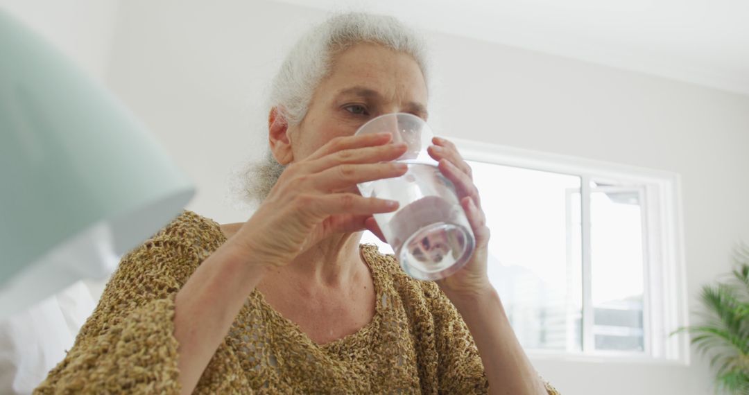 Elderly Woman Drinking Water Near Window - Free Images, Stock Photos and Pictures on Pikwizard.com