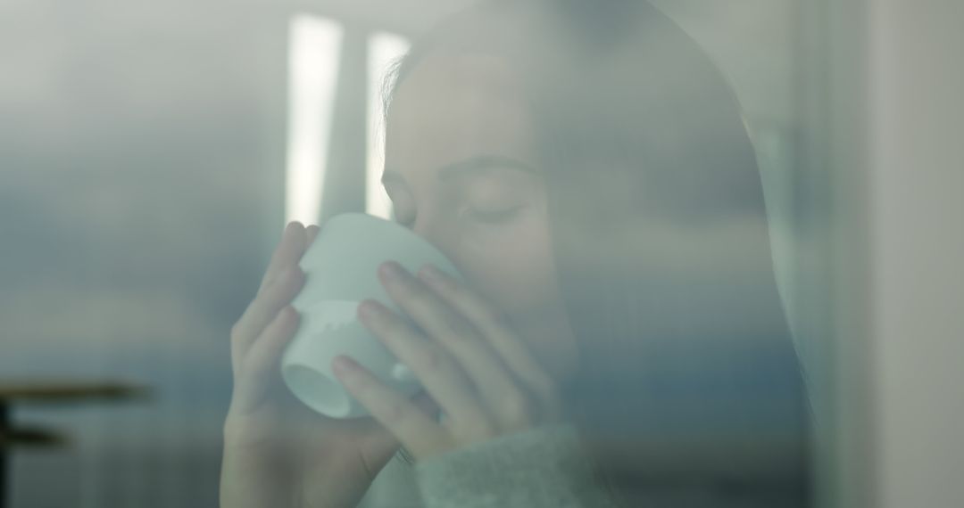 Reflective Young Woman Enjoying Hot Beverage by Window - Free Images, Stock Photos and Pictures on Pikwizard.com