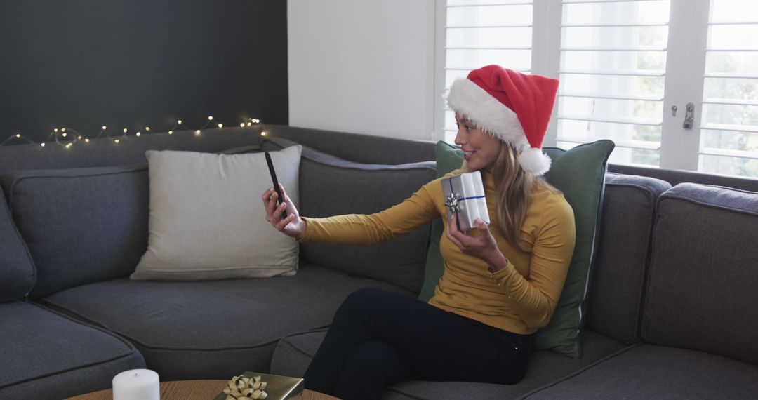 Woman Wearing Santa Hat Holding Gift During Video Call on Sofa - Free Images, Stock Photos and Pictures on Pikwizard.com