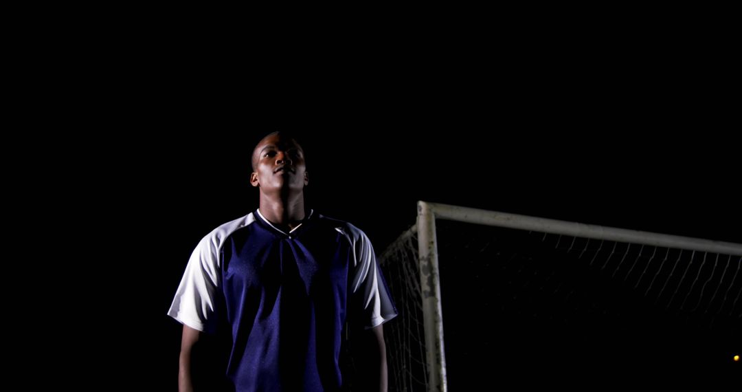 Soccer Goalkeeper Standing on Field at Night with Goal Post Behind