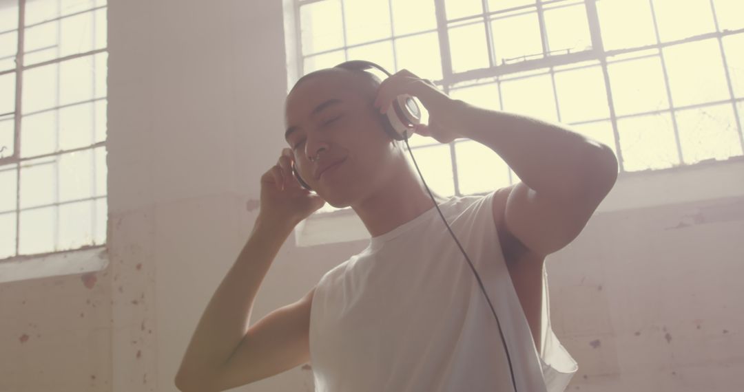 Young Person Enjoying Music with Headphones Near Large Windows - Free Images, Stock Photos and Pictures on Pikwizard.com