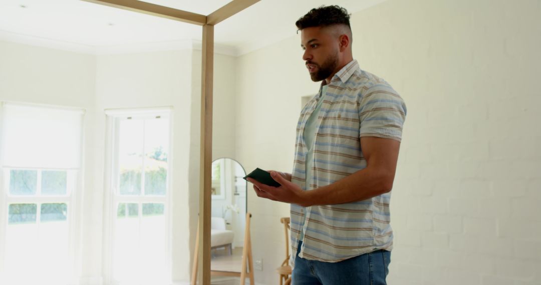 Man Holding Smartphone Standing by Mirror in Bright Home