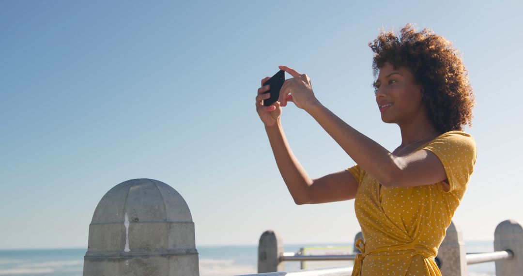 Woman in Yellow Dress Taking Selfie on Sunny Seaside Promenade - Free Images, Stock Photos and Pictures on Pikwizard.com