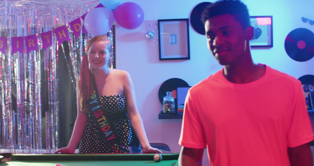 Celebrating birthday during retro game night with woman wearing sash leaning on pool table