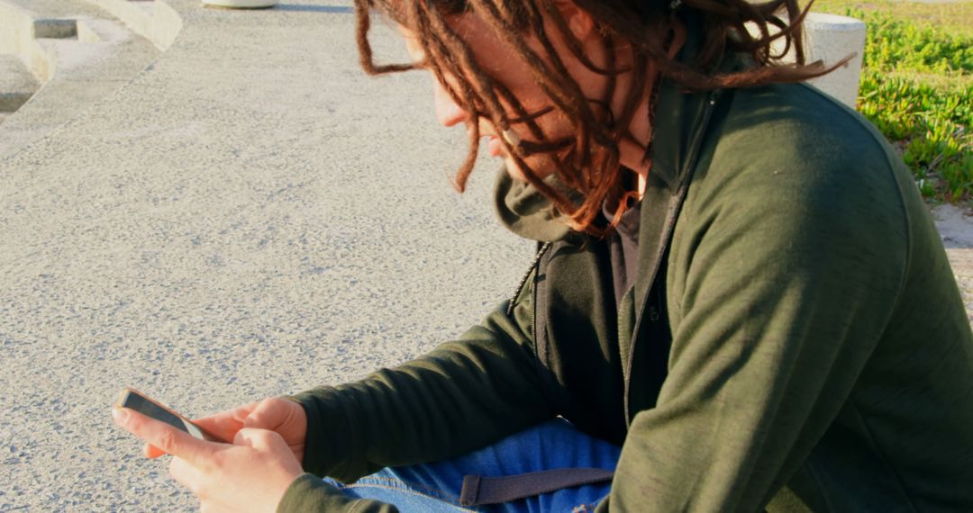 Young Person with Dreadlocks Using Smartphone Outdoors - Free Images, Stock Photos and Pictures on Pikwizard.com