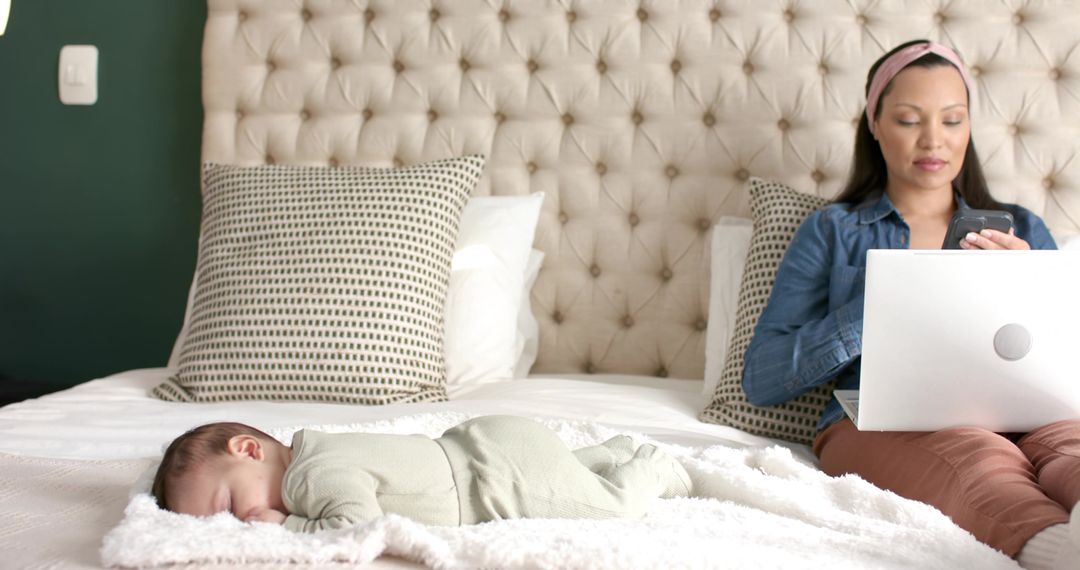 Mother Multitasking with Infant Sleeping Nearby on Bed