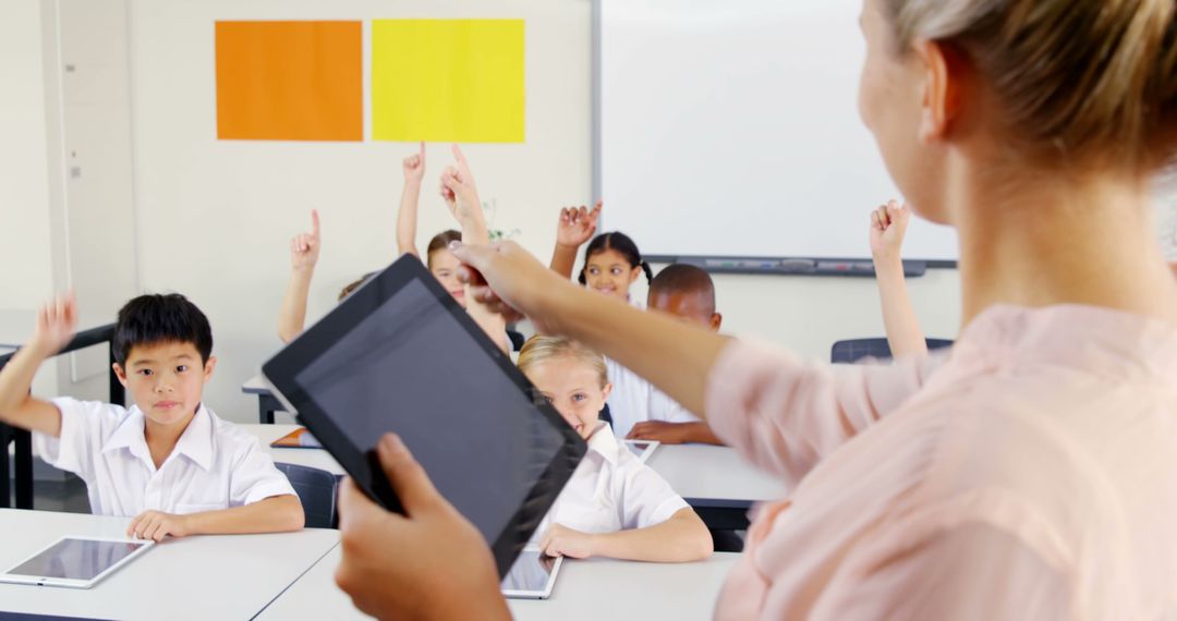 Teacher using tablet leading classroom activity with students raising hands - Free Images, Stock Photos and Pictures on Pikwizard.com