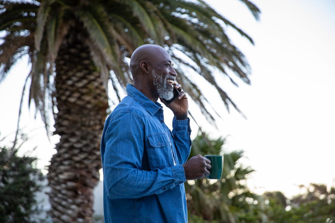 Senior Man in Nature Enjoying Phone Call and Coffee with Palm Tree Background