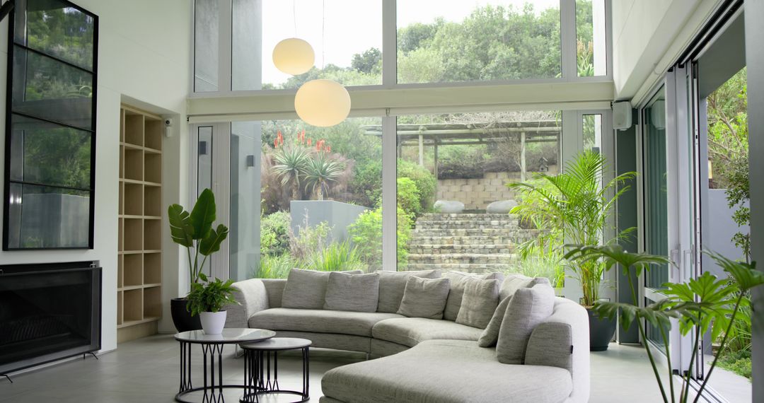 Light-gray curved sectional sofa facing floor-to-ceiling glass with lush garden view, modern minimal