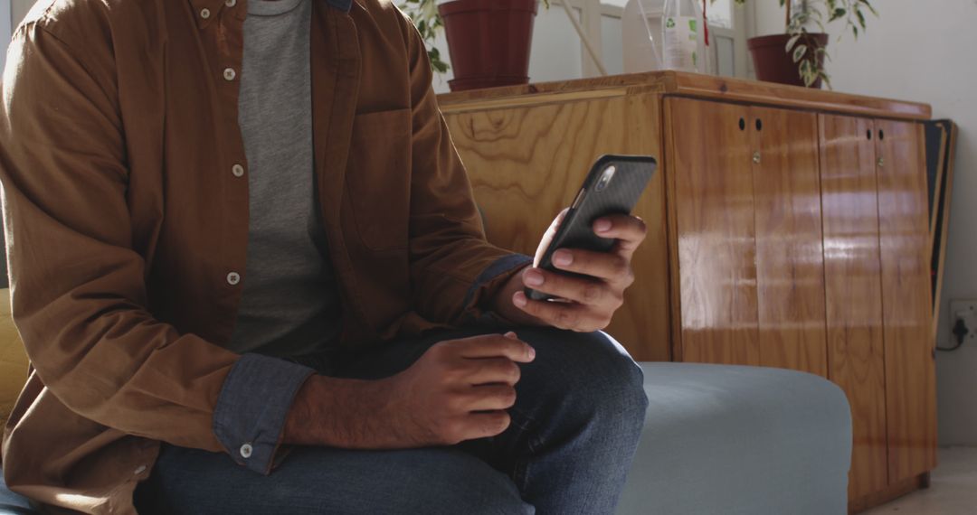 Man sitting casually using smartphone indoors - Free Images, Stock Photos and Pictures on Pikwizard.com