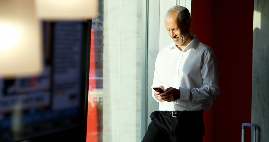 Businessman in white shirt using smartphone near large window in modern office - Free Images, Stock Photos and Pictures on Pikwizard.com