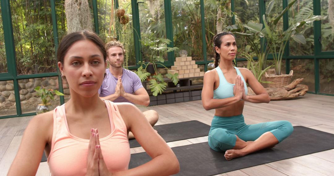 Diverse Group Practicing Yoga Meditation in Peaceful Glass House Setting