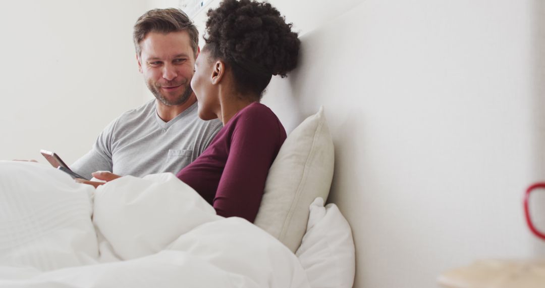 Image of happy diverse couple using tablet in bed and talking - Free Images, Stock Photos and Pictures on Pikwizard.com