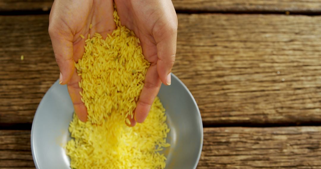 Hands Pouring Yellow Rice into Bowl on Rustic Wooden Table - Free Images, Stock Photos and Pictures on Pikwizard.com