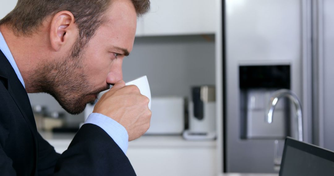 Businessman Drinking Coffee While Working on Laptop in Kitchen - Free Images, Stock Photos and Pictures on Pikwizard.com