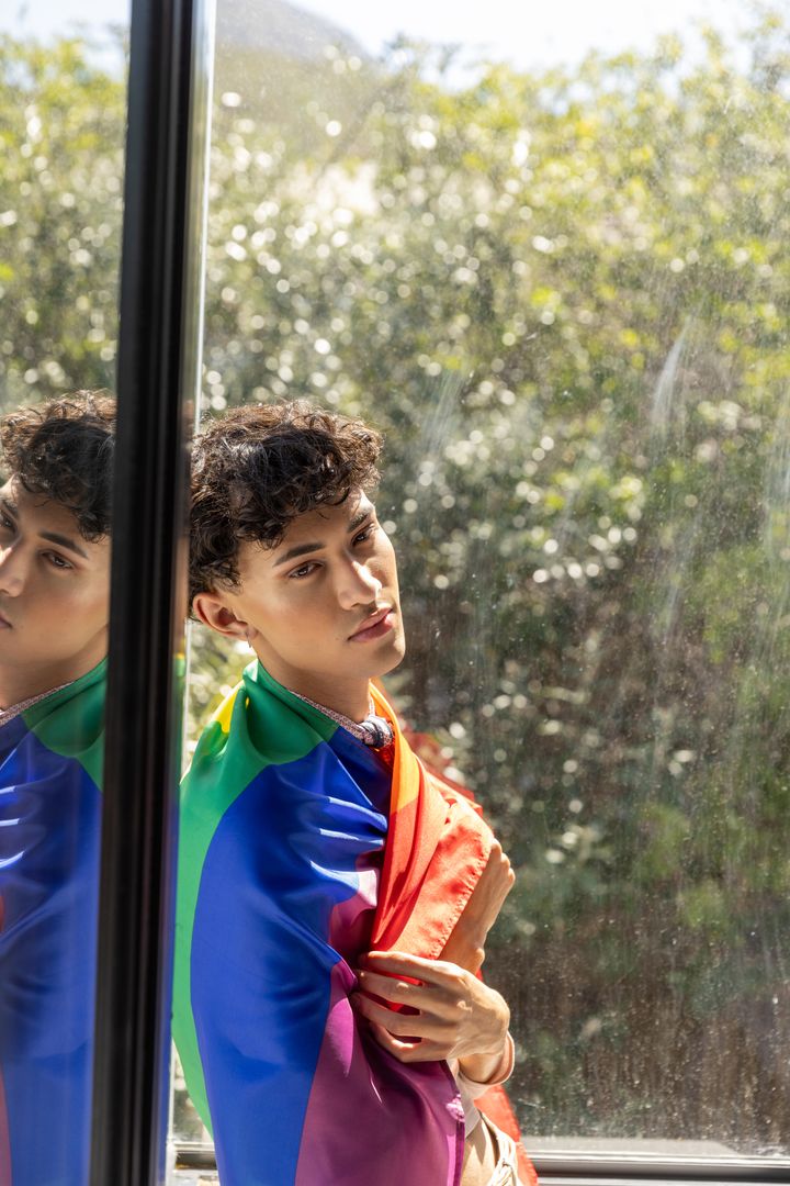 Contemplative LGBTQ Young Man in Natural Light Wrapped in Pride Flag