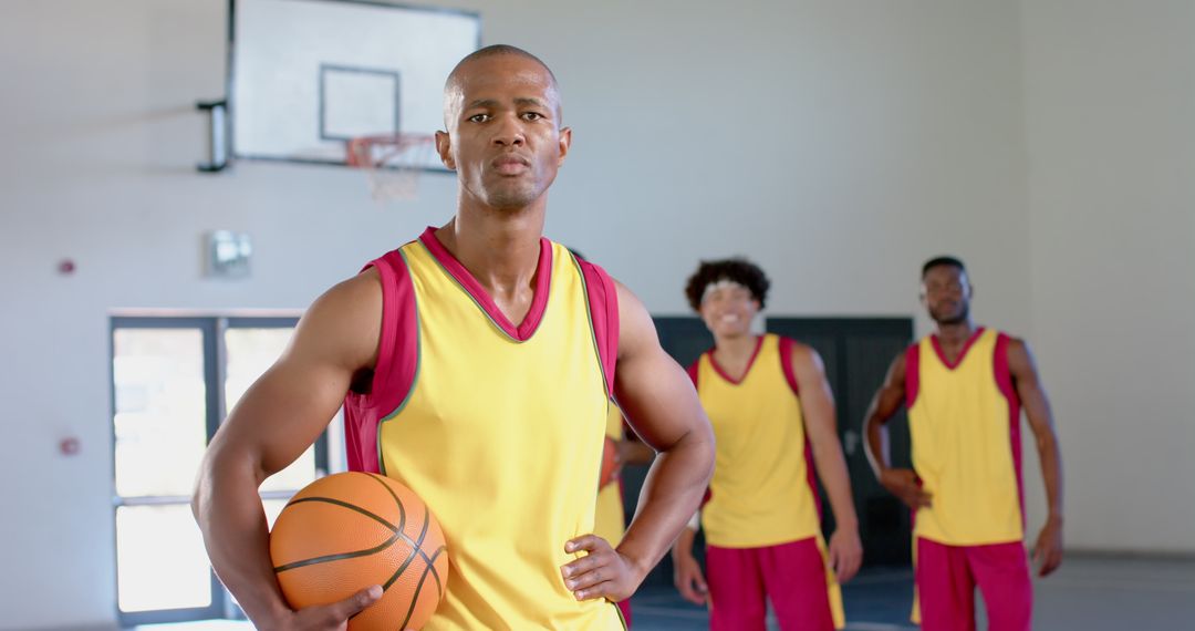 Confident Basketball Player Holding Ball with Teammates in Gym