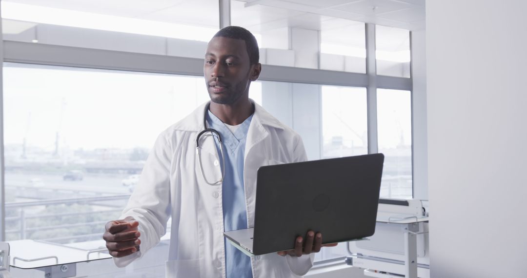 African American Male Doctor Holding Laptop in Modern Hospital - Free Images, Stock Photos and Pictures on Pikwizard.com