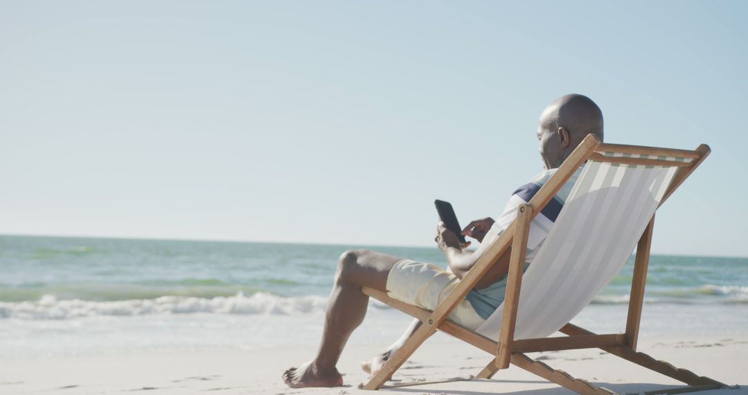 Relaxed Man Sitting in Beach Chair Using Smartphone on Sunny Day - Free Images, Stock Photos and Pictures on Pikwizard.com