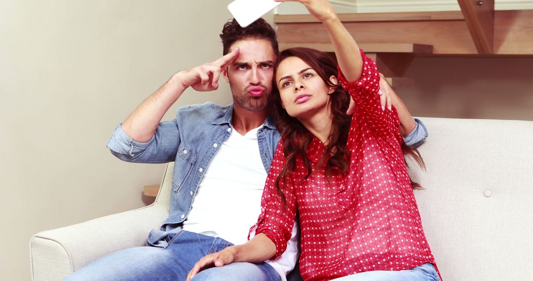 Happy Couple Taking a Humorous Selfie on Sofa Indoors