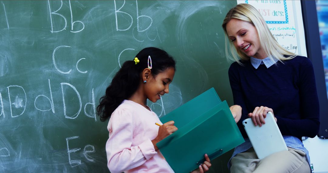 Teacher Helping Young Student With Assignment Near Chalkboard Classroom - Free Images, Stock Photos and Pictures on Pikwizard.com